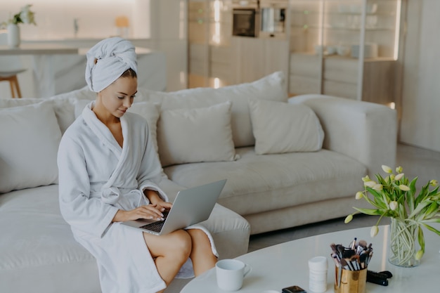 Photo of beautiful young woman in bathrobe types on laptop computer