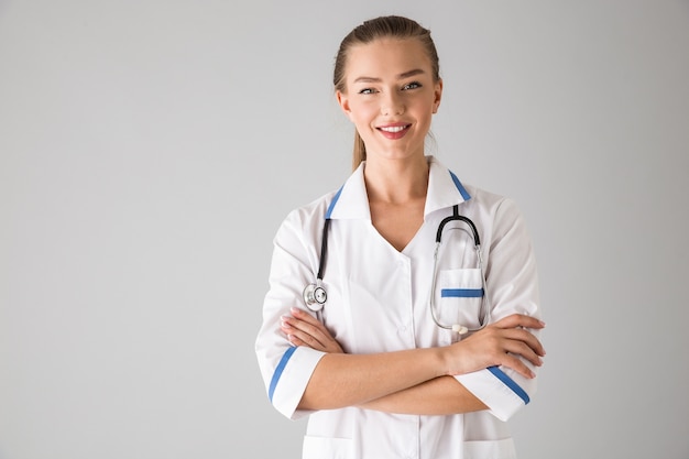 Photo of a beautiful young woman cosmetologist doctor isolated over grey wall .