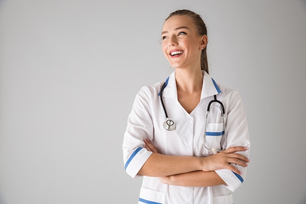 Photo of a beautiful young woman cosmetologist doctor isolated over grey wall .