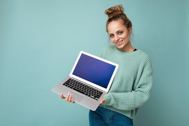 Photo of beautiful young woman holding computer laptop looking at camera isolated over colourful background