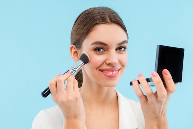 Photo of beautiful young woman posing isolated holding makeup brush and mirror.