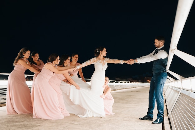 Photo of bridesmaids grabbing the bride and groom pulling her