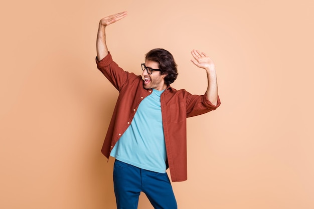 Photo of carefree guy open raise arms open mouth dance wear eyewear brown t-shirt isolated beige color background