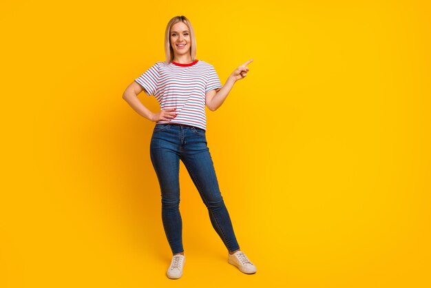 Photo of charming sweet young woman dressed shirt smiling pointing finger empty space isolated yellow color background