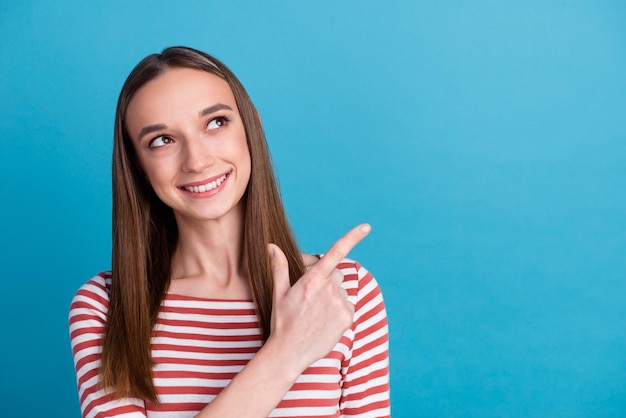 Photo of charming young woman dressed shirt smiling pointing finger empty space isolated blue color background