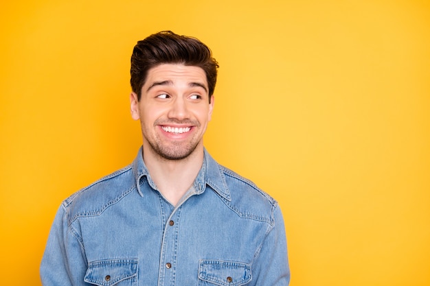 Photo of cheerful attractive man smiling toothily looking into empty space with bristle on face isolated yellow vivid color wall