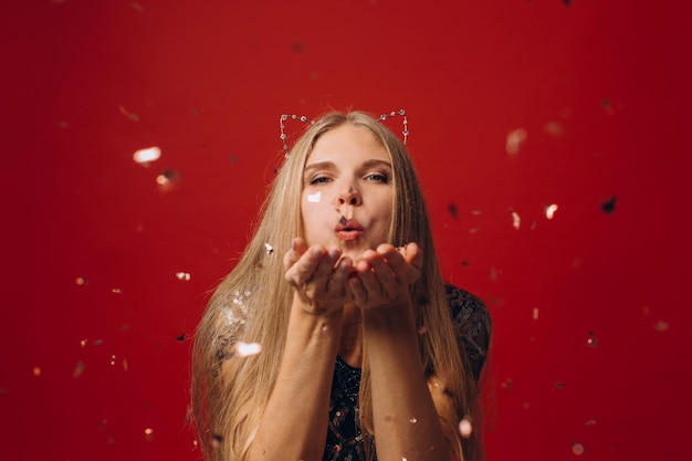 Photo of cheerful pretty woman blowing gold confetti from hands isolated on red background