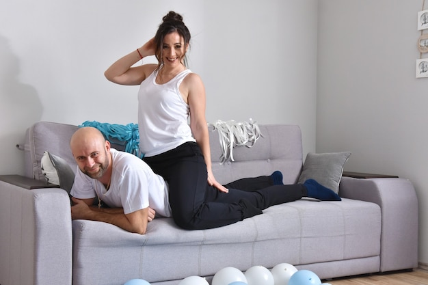 Photo of cheerful romantic caucasian family couple smiling and hugging while sitting on sofa at home. Man and woman in love