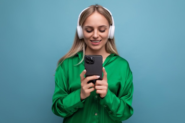 Photo of a cute attractive blonde young woman in headphones with a smartphone in her hands on a blue