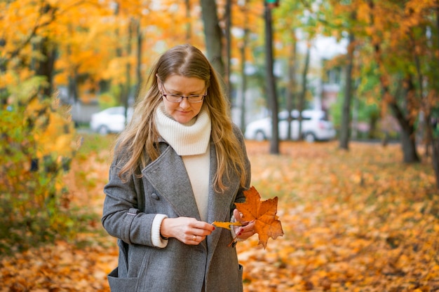 Photo of a cute blonde lady, yellowed falling leaves, a walk and a beautiful unforgettable scent of autumn, city park, on the street