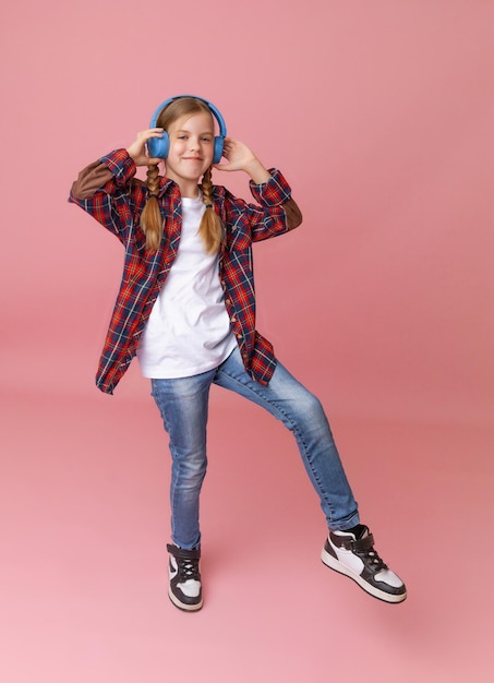 Photo of a cute funny young teenage girl in a pink jumper headphones dancing enjoying music on a background