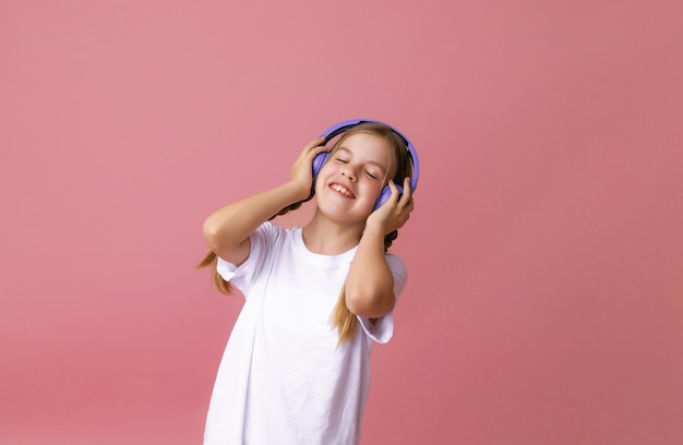 Photo of a cute funny young teenage girl in a pink jumper headphones dancing enjoying music on a background