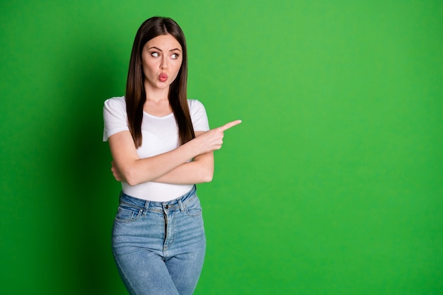 Photo of cute sweet woman dressed casual white t-shirt arms crossed pointing looking empty space lips pouted isolated green color background