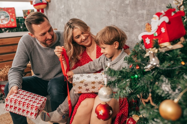 Photo of Dad, mom and son. Spending time. Christmas tree at home has happy moments. Preparing for holiday. Family with one child. Happiness. Have fun. red green decore