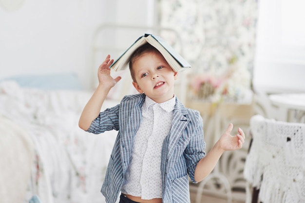 Photo of diligent schoolboy with book on his head doing homework. The schoolboy is tired of doing homework