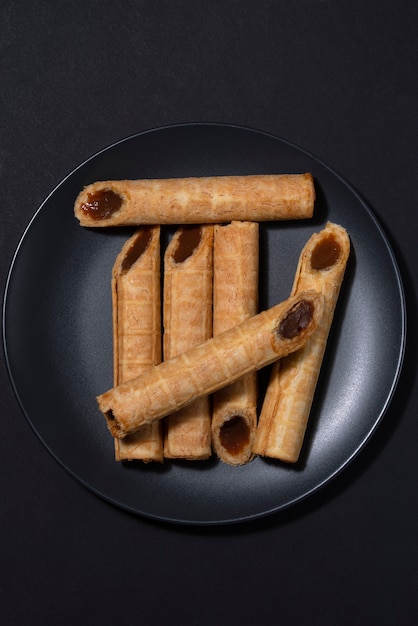 Photo of a dish with homemade waffle rolls with boiled condensed milk and nuts on a black plate