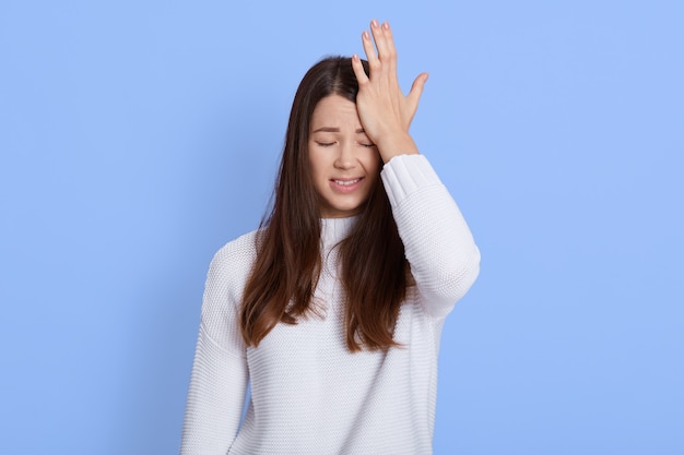 Photo of dissatisfied young woman regrets wrong doing, keeps hand on forehead