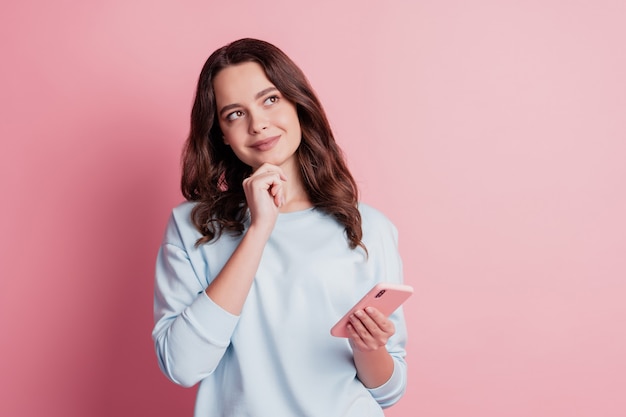 Photo of dreamy girl use smartphone finger chin look up empty space