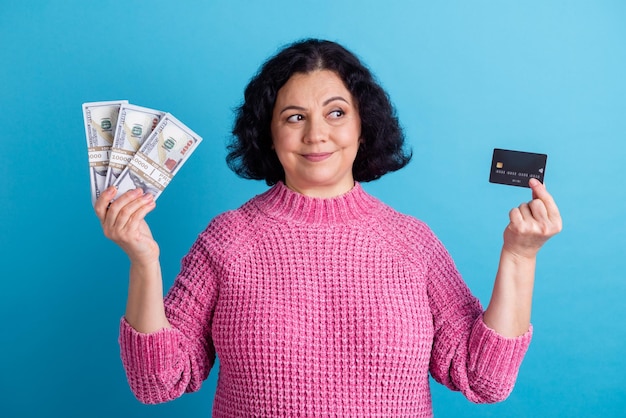 Photo of elderly woman happy positive smile hold cash money dollars credit card isolated over blue color background