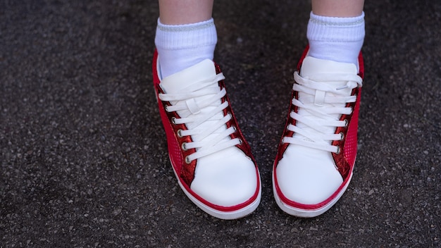 Photo of female legs in red and white sneakers on gray wet asphalt