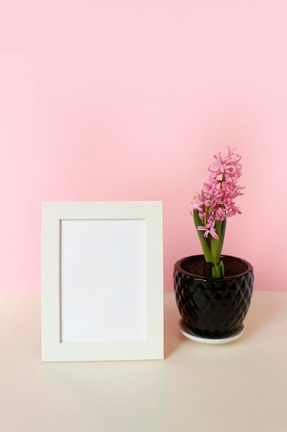 Photo frame with white blank card and flowers on pastel pink background Mock up poster frame Stylish template