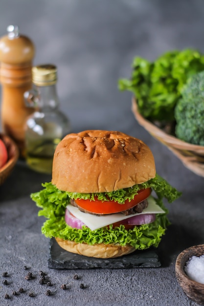 Photo of fresh burger on wooden cutting board on dark