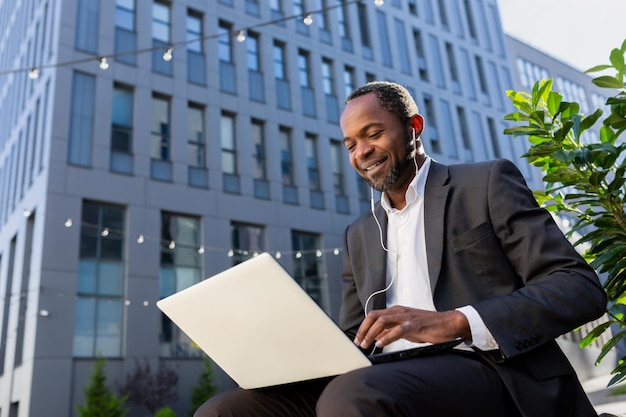 Photo from below african american man in a suit sits outside an office center on a bench on a city