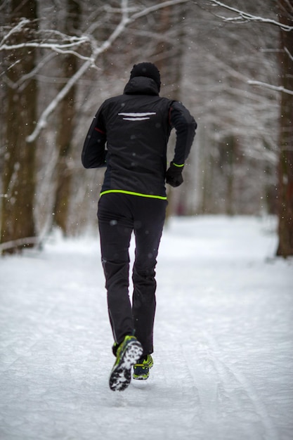 Photo from back of running athlete among trees in winter forest