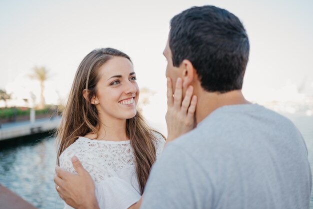 A photo from behind of a stylish man at whom his smiling girlfriend is staring and stroking his face