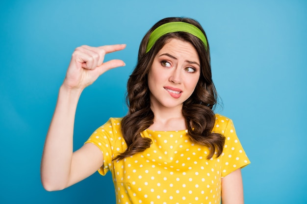 Photo of frustrated girl show product empty space tiny size with fingers isolated over blue color background