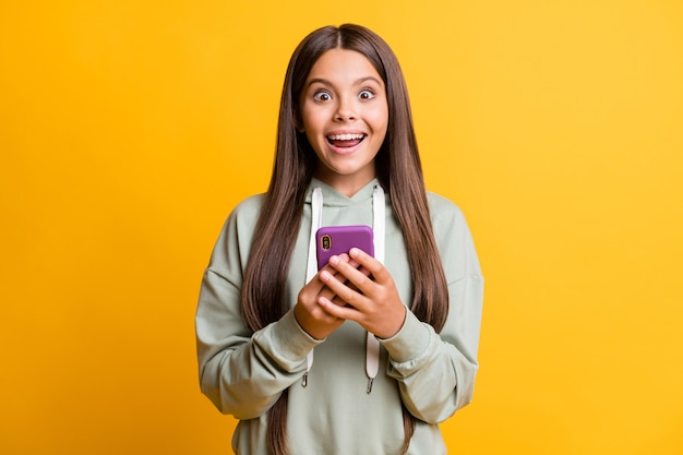 Photo of funny shocked school girl wear casual grey outfit holding hands arms modern gadget isolated yellow color background