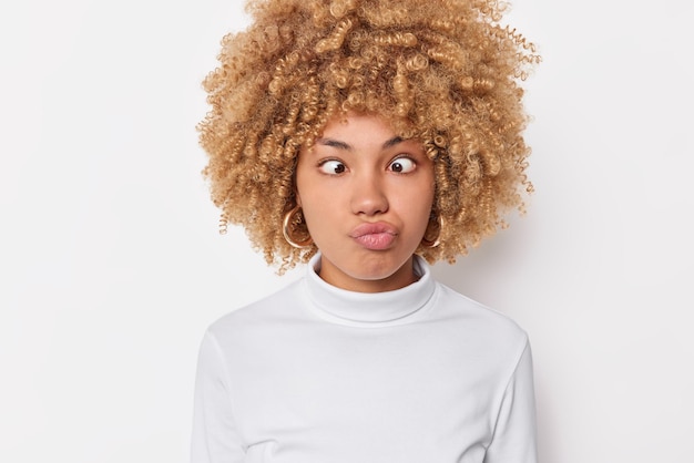 Photo of funny woman makes grimace pouts lips and crosses eyes has childish expression acts like fool dressed casually isolated over white background tries to amuse someone. Look how I can do