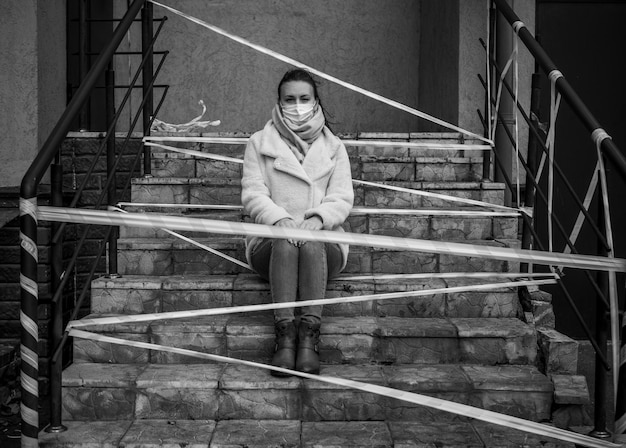 Photo of a girl in a mask Sitting on the street with danger warning tapes