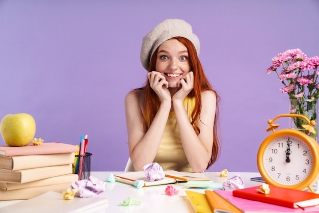 Photo of gorgeous student girl sitting at desk with exercise books while doing homework isolated over purple wall