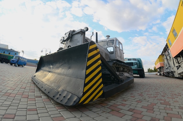 Photo of a gray bulldozer among the railway trains. Strong distortion from the fisheye lens