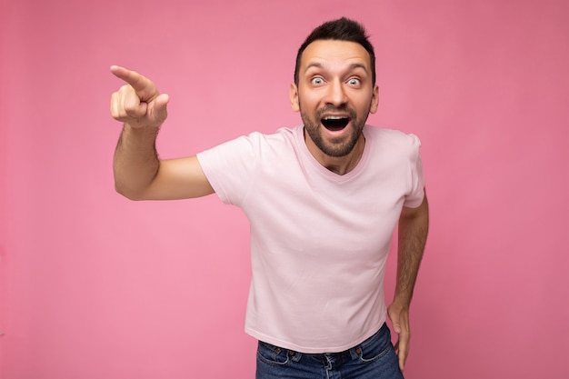 Photo of handsome emotional happy positive amazed brunet man in casual pink tshirt isolated on pink