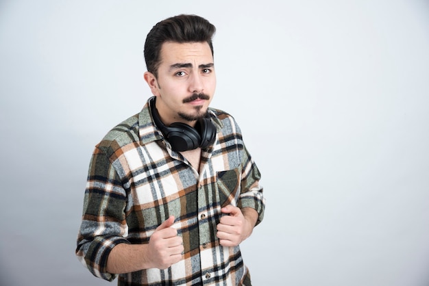 Photo of handsome man with headphones standing and looking over white wall.