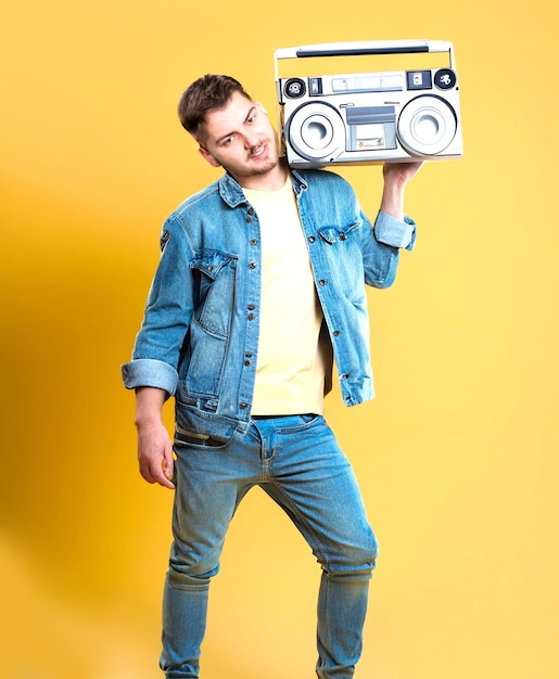 photo Handsome young man wearing jeans jacket holding boombox on yellow background