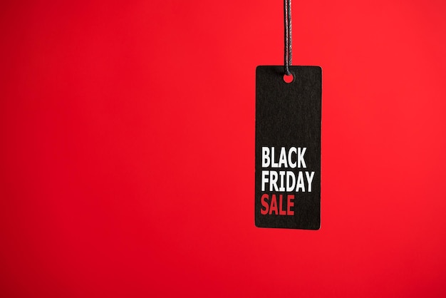 Photo of hanging black price tag on isolated red background with text