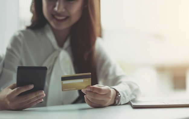 Photo of a happy Asian business woman sitting in the office using a laptop computer and a mobile phone holding a credit card