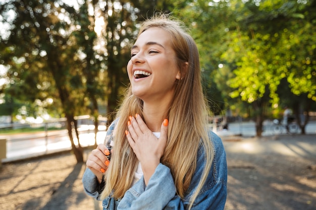 Photo of a happy laughing positive cheerful young girl walking outside in nature green park.