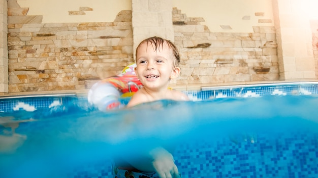 Photo of happy laughing and smiling little boy playing with toys and learning swimming in indoors swimming pool