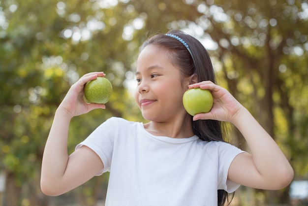 Photo happy Little asian girl child standing with big smile. holding green apple in your hand
fresh healthy green bio nature with abstract blurred foliage and bright summer sunlight