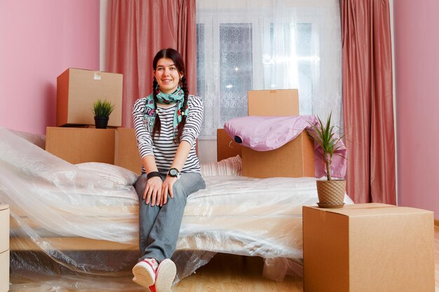 Photo of happy woman sitting on sofa among cardboard boxes