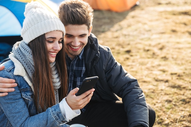 Photo of happy young loving couple outside with tent in free alternative vacation camping over mountains using mobile phone.