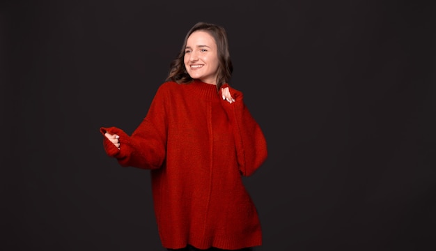 Photo of happy young woman in red sweater dancing over dark background