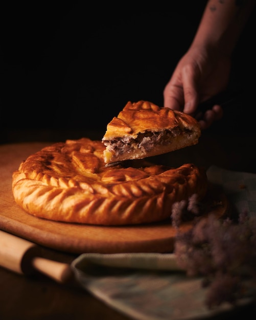 Photo of homemade meat pie in low key Dark wooden background Woman hold a piece of meat pie