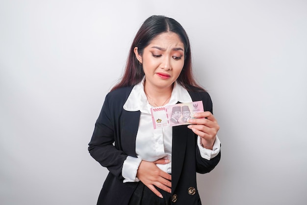 Photo of a hungry excited young businesswoman holding money in Indonesian Rupiah and wondering what to order yummy food isolated on white color background