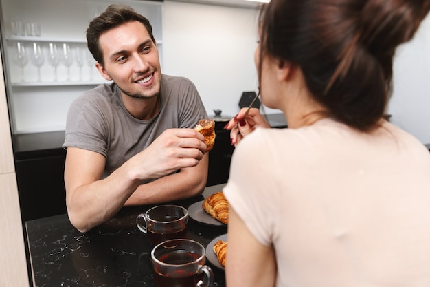 Photo of joyful couple man and woman sitting at table in flat, and having breakfast together