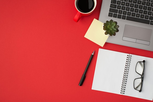 Above photo of laptop plant cup of coffee notepad glasses sticker and pen isolated on the red backdrop with blank space